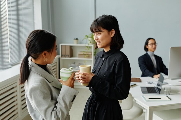 Vue latérale portrait de deux jeunes femmes d'affaires discutant tout en dégustant un café à la pause au bureau