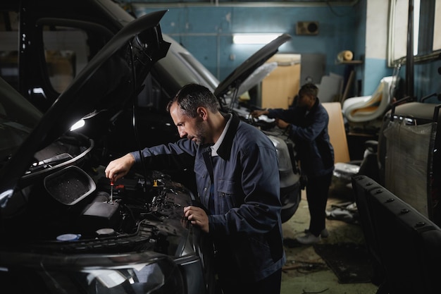 Photo vue latérale portrait de deux mécaniciens fixant des camions dans l'espace de copie d'atelier de garage