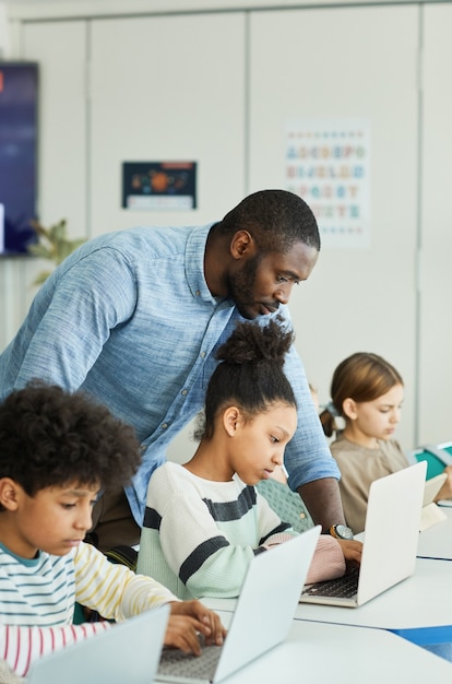 Vue Latérale Portrait D'un Enseignant Aidant Les Enfants à Utiliser Des Ordinateurs En Classe Informatique