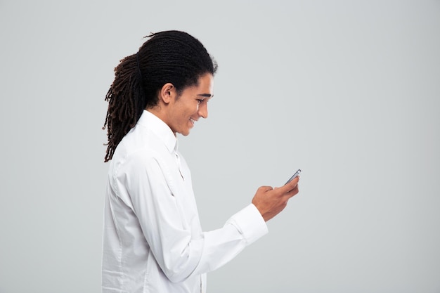 Vue latérale portrait d'un heureux homme d'affaires afro-américain à l'aide de smartphone sur mur gris