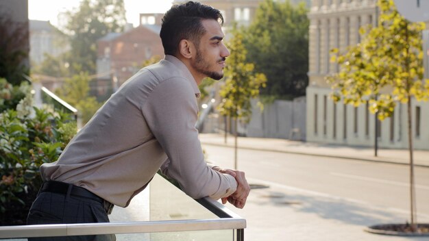 Vue latérale portrait homme d'affaires hispanique détendu debout à la balustrade moderne gratte-ciel immeuble de bureaux regardant loin sur la rue de la ville pensant au repos Gros plan homme réussi homme sur balcon terrasse