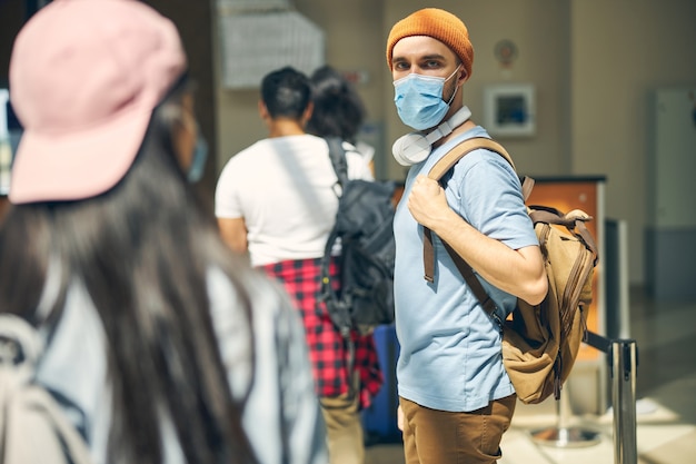 Vue latérale portrait d'un homme barbu portant un masque de protection avec sac à dos sur l'épaule posant devant l'appareil photo