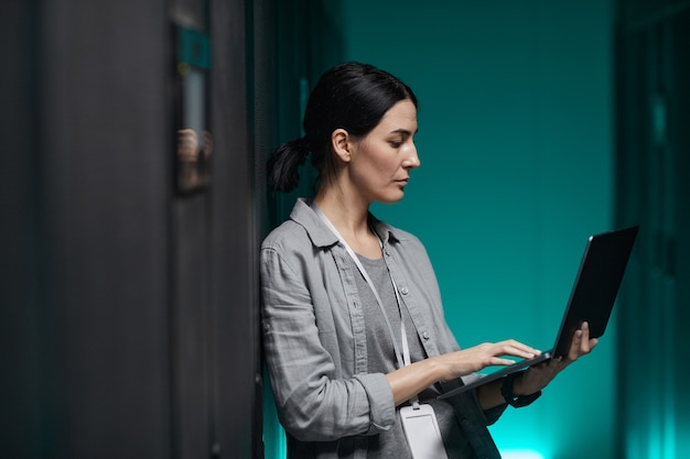 Vue latérale portrait d'une ingénieure en données tenant un ordinateur portable tout en travaillant avec un superordinateur dans la salle des serveurs, espace de copie