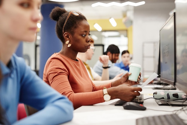 Photo vue latérale portrait d'une jeune femme noire à l'aide d'un ordinateur dans la bibliothèque du collège tout en faisant des recherches pour e