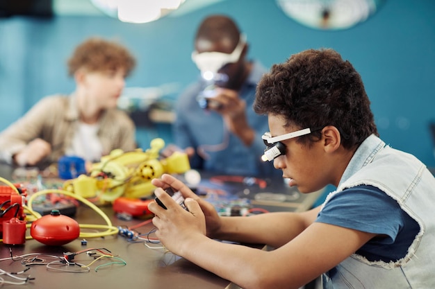 Vue latérale portrait d'un jeune garçon noir construisant des robots en classe d'ingénierie à l'espace de copie de l'école