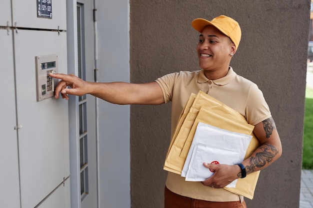 Vue latérale portrait d'une livreuse sonnant à la porte et tenant des colis