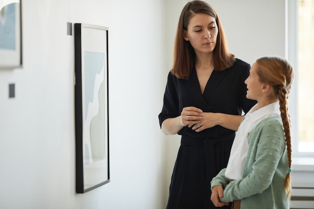 Vue latérale portrait de la mère et de la fille visitant ensemble une galerie d'art moderne et regardant des photos, espace de copie