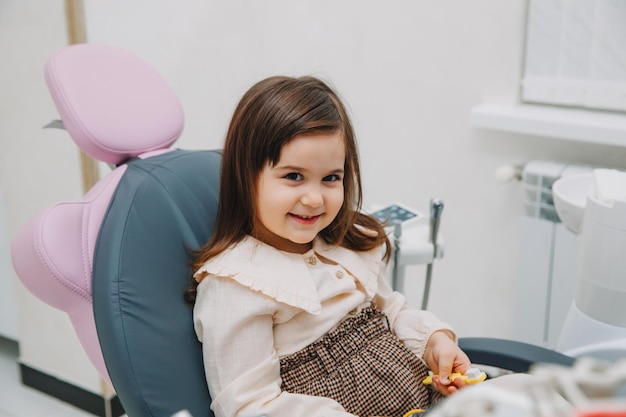 Vue latérale portrait d'une petite fille regardant un miroir en dentisterie pédiatrique après une chirurgie dentaire.