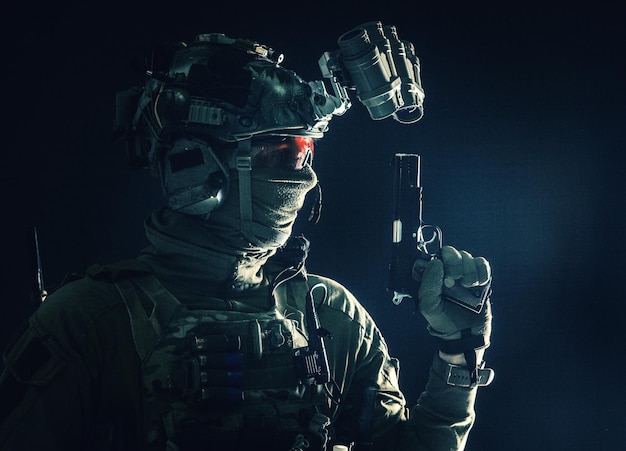 Photo vue latérale portrait d'un soldat de l'armée combattant moderne combattant des forces spéciales dans un casque radio avec dispositif de vision nocturne cachant l'identité derrière un masque pistolet de service armé tournage en studio discret
