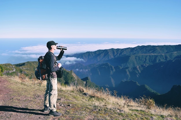 Vue latérale d'un randonneur buvant de l'eau sur la montagne contre le ciel bleu