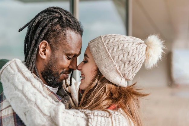 Vue latérale rapprochée d'un couple multiracial souriant touchant avec le nez à l'extérieur