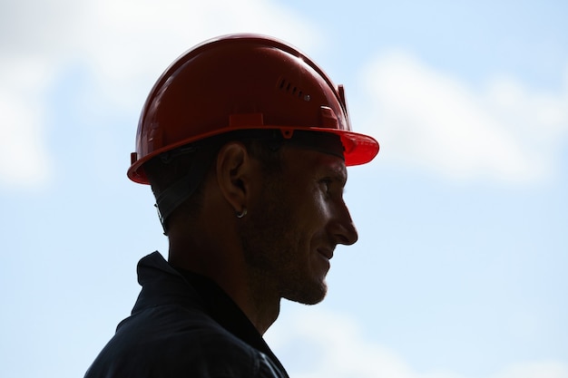 Vue latérale rétroéclairée d'un travailleur de la construction portant un casque de protection en se tenant debout contre le ciel en arrière-plan, espace pour copie