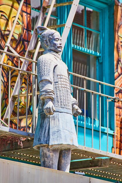 Vue latérale d'une statue d'homme chinois debout devant une fresque murale de soldat