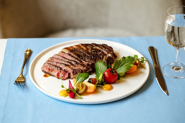 Vue latérale sur le steak de boeuf faux-filet avec salade de légumes frais sur la table bleue