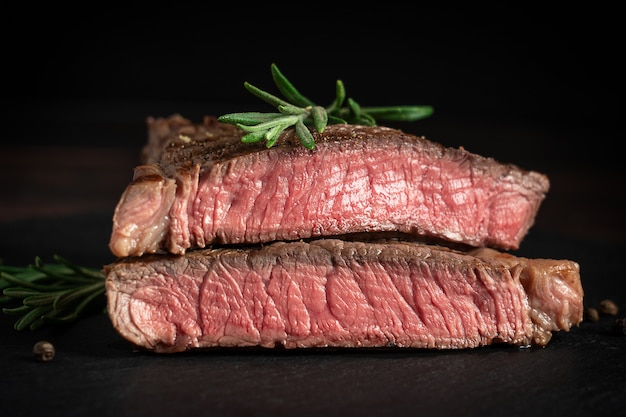 Vue latérale d'un steak rôti juteux tranché en deux parties à base de viande de boeuf nourrie au grain avec du romarin