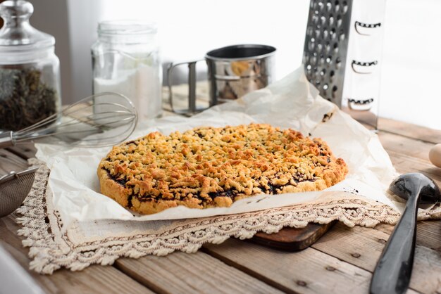 Vue latérale de la tarte entière râpée sur une feuille de papier sulfurisé entourée d'ustensiles de cuisine sur une table en bois