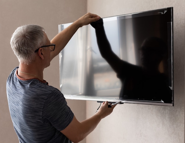 Vue latérale d'un technicien mature installant la télévision à la maison