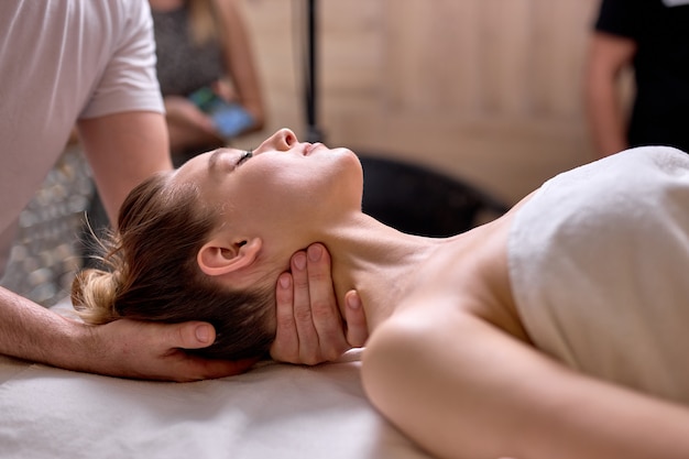 Vue latérale sur un thérapeute professionnel recadré faisant un massage sain sur le cou et les épaules à une cliente allongée sur le dos, vue latérale. au spa