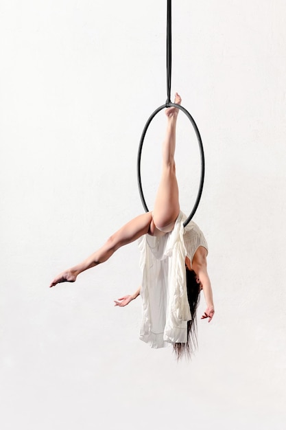 Vue latérale de tout le corps d'une femme acrobatique pieds nus mince et flexible exerçant sur un cerceau aérien sur fond blanc en studio léger