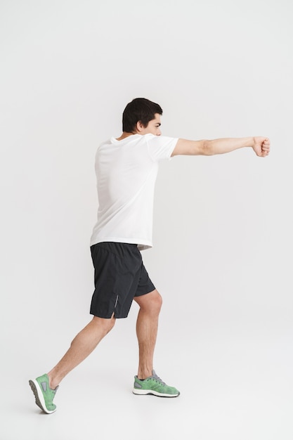 Vue latérale sur toute la longueur d'un jeune sportif confiant faisant des exercices de boxe sur blanc