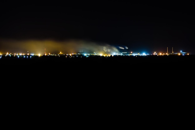 Vue sur les lumières de la ville la nuit. La fumée des cheminées de l'usine s'élève vers le ciel. Notion de pollution de l'environnement