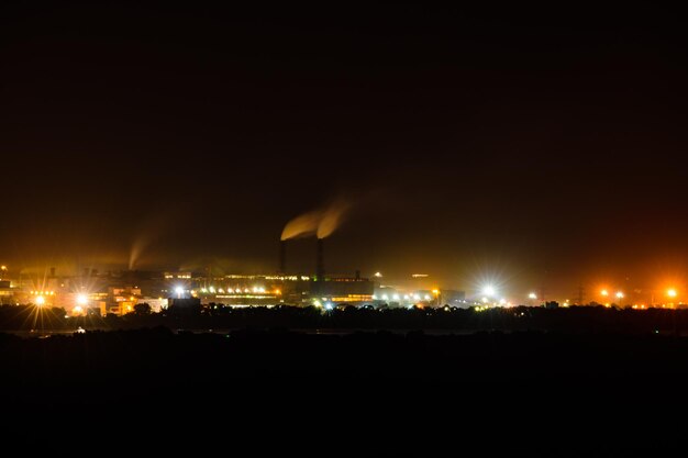 Vue sur les lumières de la ville la nuit. La fumée des cheminées de l'usine s'élève vers le ciel. Notion de pollution de l'environnement