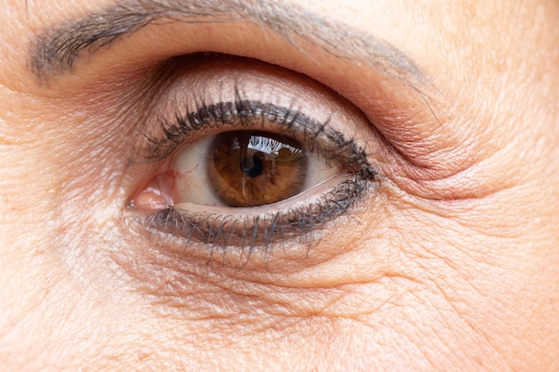 Une vue macro rapprochée sur l'œil brun d'une femme âgée avec des rides et des pattes de corbeau