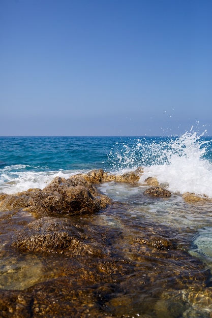 Une vue magnifique sur la mer Méditerranée bleue. Rochers ensoleillés, vagues avec mousse et éclaboussures d'eau. La vague s'écrase sur les rochers sur le rivage