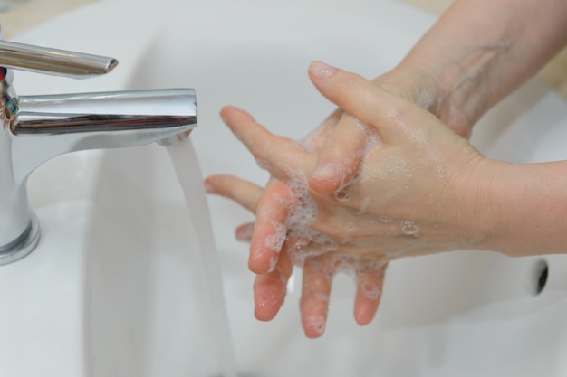 Vue des mains féminines en mousse savonneuse sous gros plan de l'eau du robinet