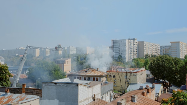 Vue de la maison en feu et des pompiers essayant d'éteindre le feu depuis un camion à plate-forme. Pompiers utilisant de l'eau pour éteindre les flammes et la fumée du bâtiment en feu, aidant en cas d'accident