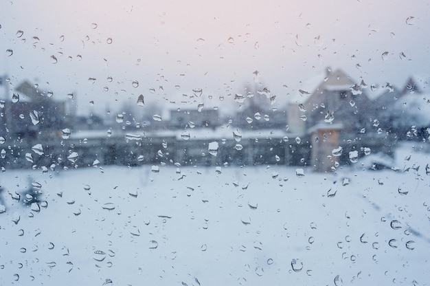 Vue des maisons à travers une fenêtre avec des gouttes de pluie