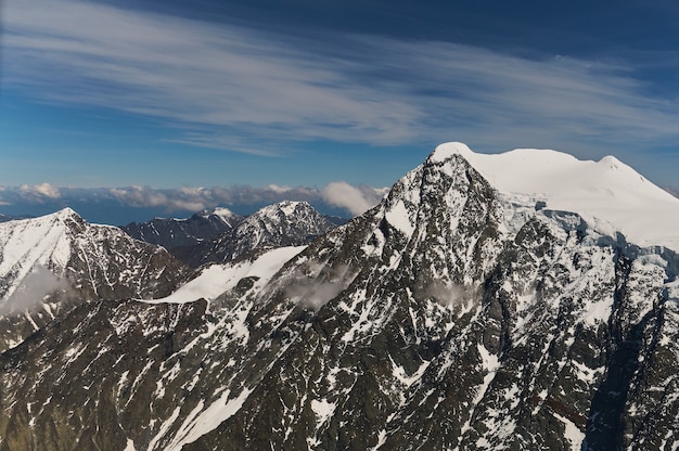 Vue minimaliste du mur de montagne enneigé dans d'épais nuages bas au soleil. Paysage de montagne lumineux pittoresque avec un pic de neige blanche parmi des nuages denses dans un ciel bleu. Magnifique paysage avec sommet enneigé.