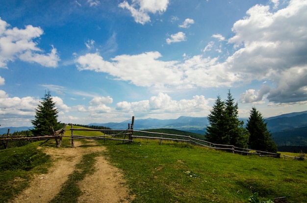 Vue sur la montagne avec clôture en bois ciel bleu nuages blancs vallée verte