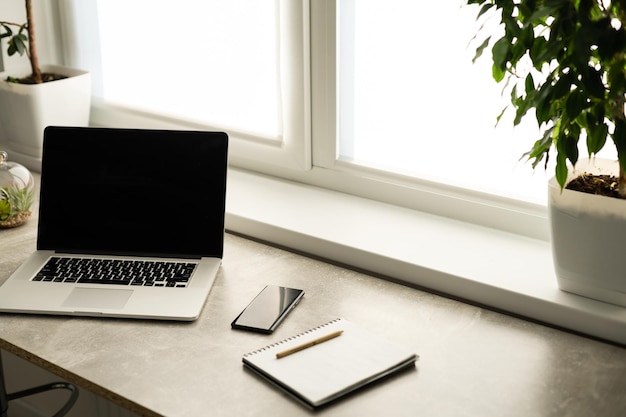 Vue de la nature morte de la salle de bureau avec ordinateur portable ouvert sur le bureau avec reflets par une fenêtre lumineuse, intérieur du bureau avec paperasse et lunettes. Technologie de travail professionnelle à l'intérieur.