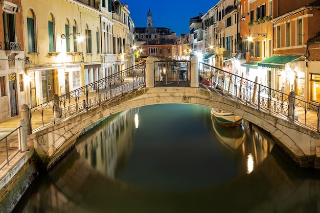 Vue nocturne de l'architecture ancienne illuminée, des bateaux flottants et des reflets lumineux dans l'eau des canaux à Venise, Italie