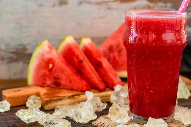 Vue normale d'un grand verre avec un smoothie froid à la pastèque et quelques triangles de waterme