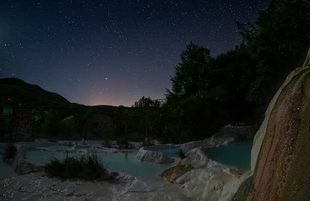 Vue de nuit : piscine géothermique et source chaude en Toscane, Italie. Cascade thermale naturelle de Bagni San Filippo le soir au clair de lune et étoiles dans le ciel.