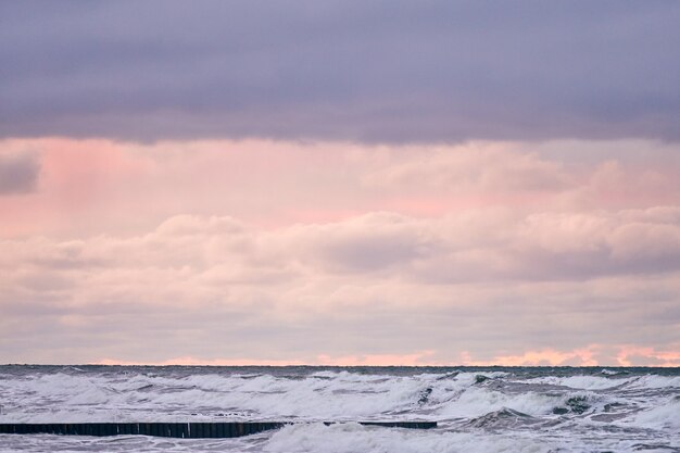 Vue panoramique sur le ciel nuageux violet et la mer avec des vagues écumantes. Vintage longs brise-lames en bois s'étendant loin vers la mer. Temps venteux, beau paysage de la mer Baltique en soirée.