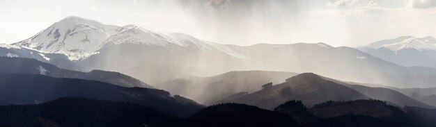 Photo vue panoramique à couper le souffle sur les magnifiques montagnes brumeuses des carpates, recouvertes d'une forêt toujours verte le matin ou le soir brumeux et calme sous un ciel sombre et nuageux. montagnes couvertes de neige sommets à distance.