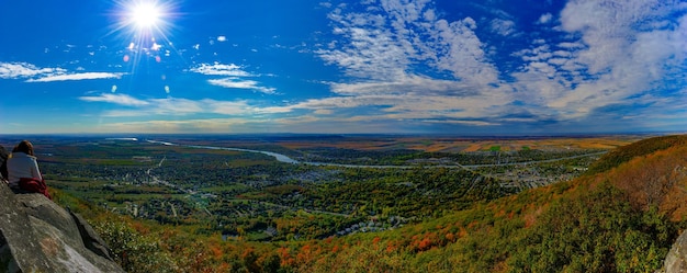 Photo vue panoramique d'une femme assise sur un rocher contre un ciel nuageux pendant une journée ensoleillée