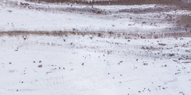 Vue panoramique d'en haut sur la texture du chemin de terre en gravier couvert de neige dans la forêt