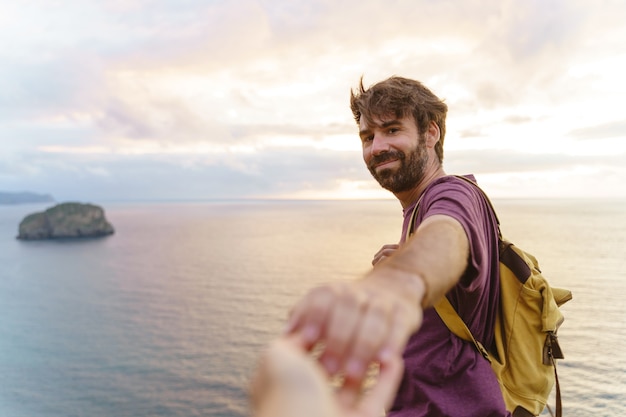 Photo vue panoramique d'un homme de race blanche avec les bras grands ouverts au coucher du soleil dans une falaise. vue horizontale du routard voyageant à l'extérieur avec l'océan bleu en arrière-plan. concept de personnes et de voyage.