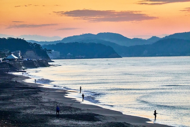 Vue panoramique de la mer avec des silhouettes de personnes contre le ciel au lever du soleil