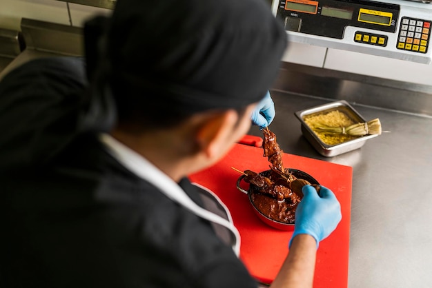 Vue par-dessus l'épaule d'un cuisinier professionnel couvrant la viande sur un bâton avec de la sauce