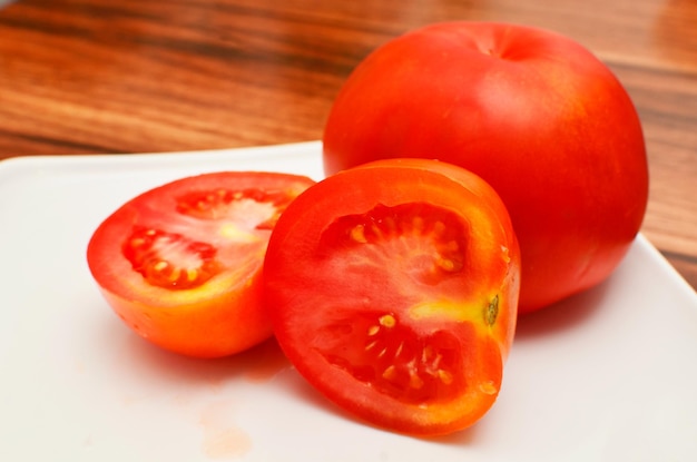 Vue d'une partie d'une assiette blanche avec des tranches et la moitié d'une tomate rouge fraîche avec vue latérale.