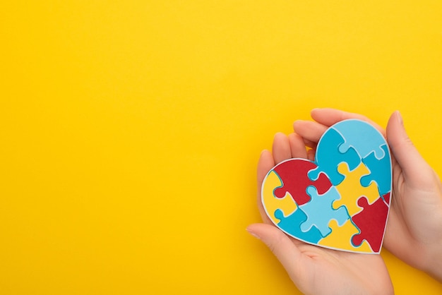 Vue partielle d'une femme tenant un coeur de puzzle coloré sur jaune pour la Journée mondiale de sensibilisation à l'autisme