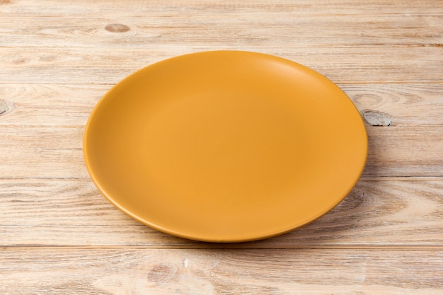 Vue de perspective. Assiette mate jaune vide sur un fond en bois orange