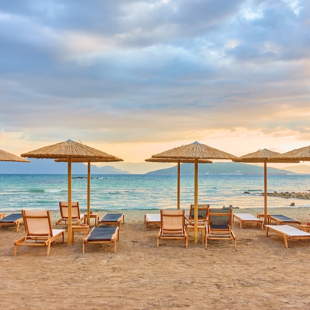 Photo vue pittoresque sur la plage avec des rangées de parasols en paille au bord de la mer au coucher du soleil