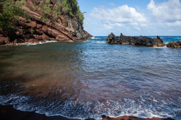 Vue sur la plage de la mer avec des vagues et la plage de sable rouge de la côte rocheuse à Maui en hawaïen