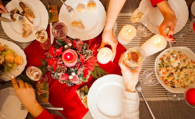 Vue à plat de la table avec décoration de Noël, repas savoureux, bougies, champagne et mains de femmes tenant des fourchettes et des couteaux. dîner de Noël